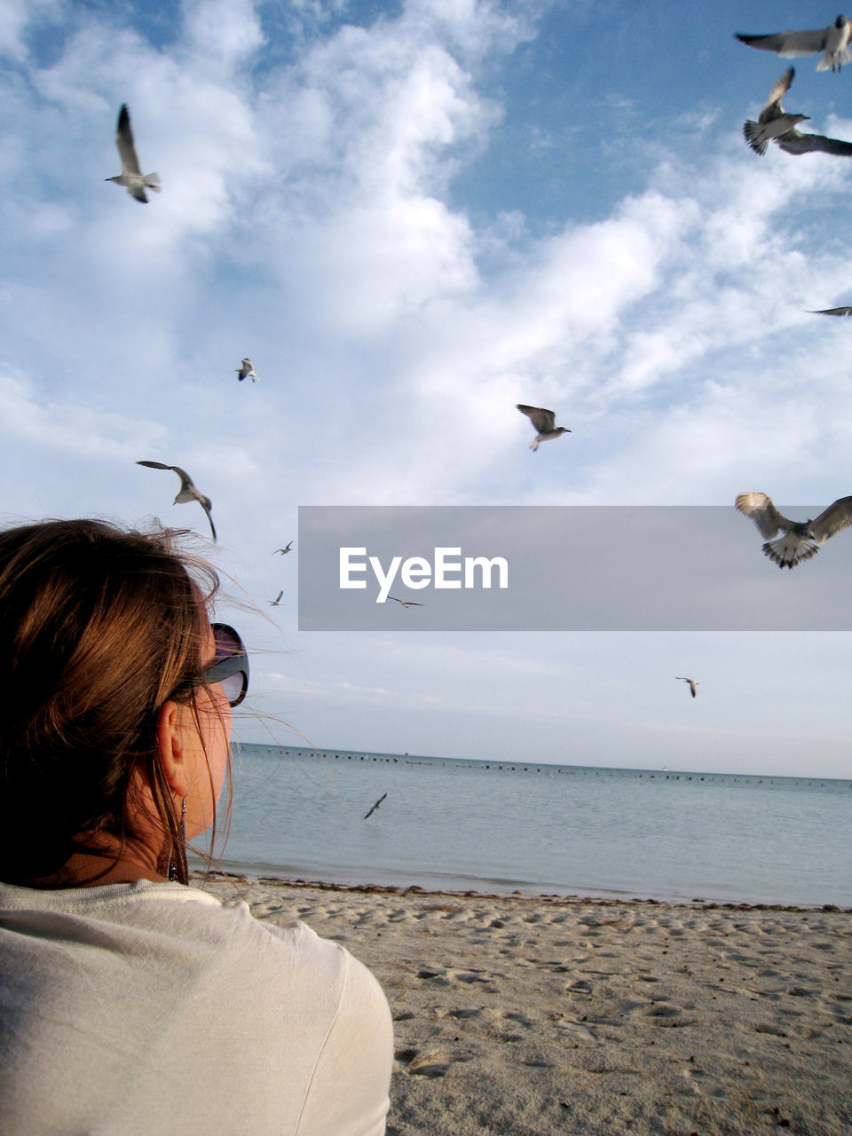 Rear view of woman looking at seagulls flying against sky