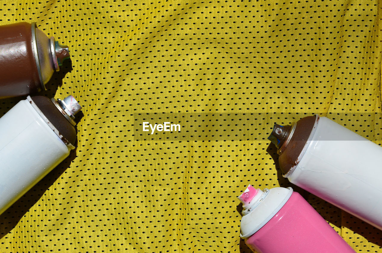 High angle view of spray cans on yellow fabric