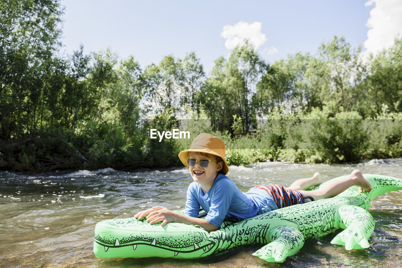 Boy wearing bucket hat lying on inflatable crocodile