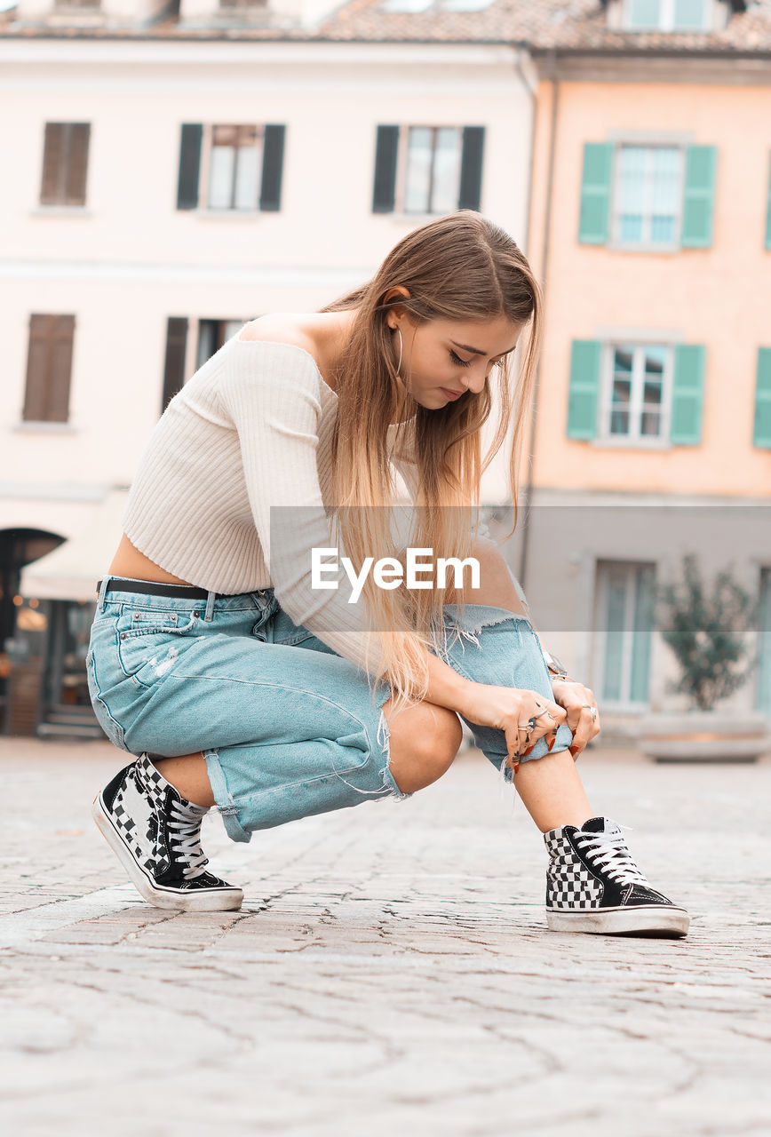 Full length of young woman crouching in city