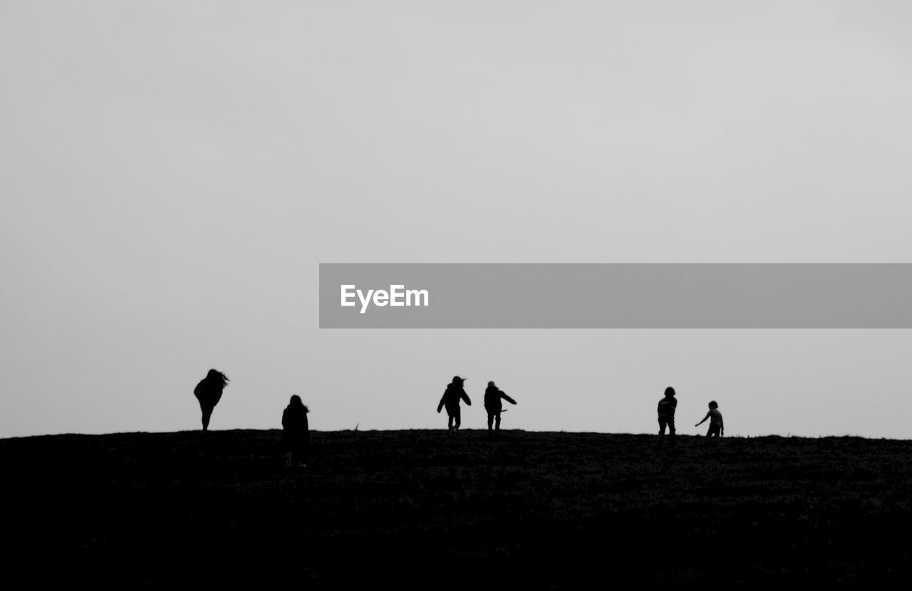 Silhouette people enjoying on field against clear sky