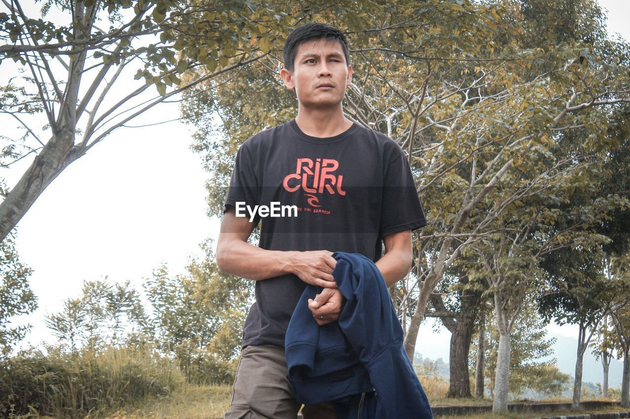 PORTRAIT OF A YOUNG MAN STANDING ON TREE