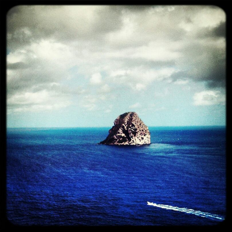 Large rock amidst blue sea against cloudy sky