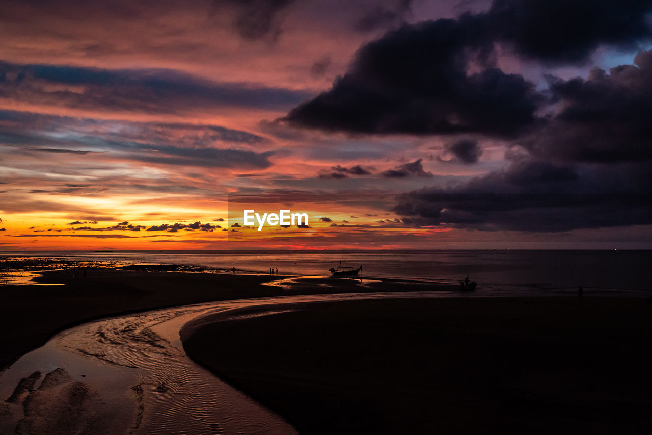 Scenic view of beach against cloudy sky during sunset