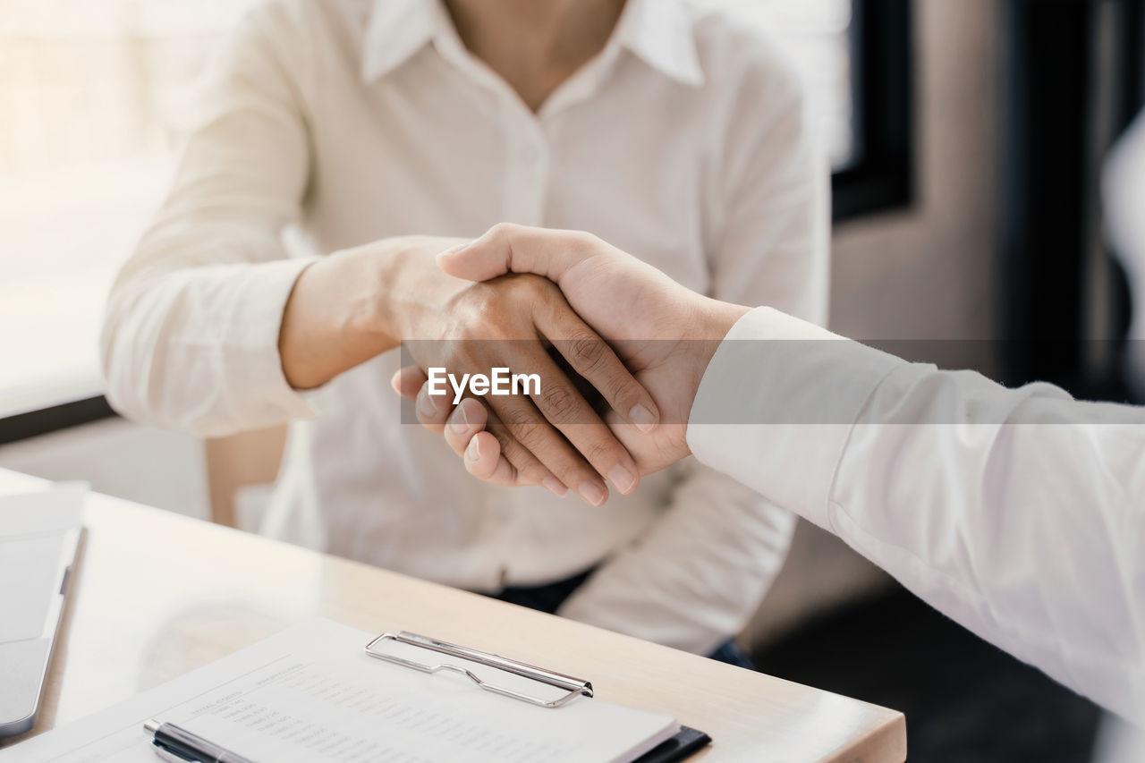 Close-up of man with female coworker shaking hands in office