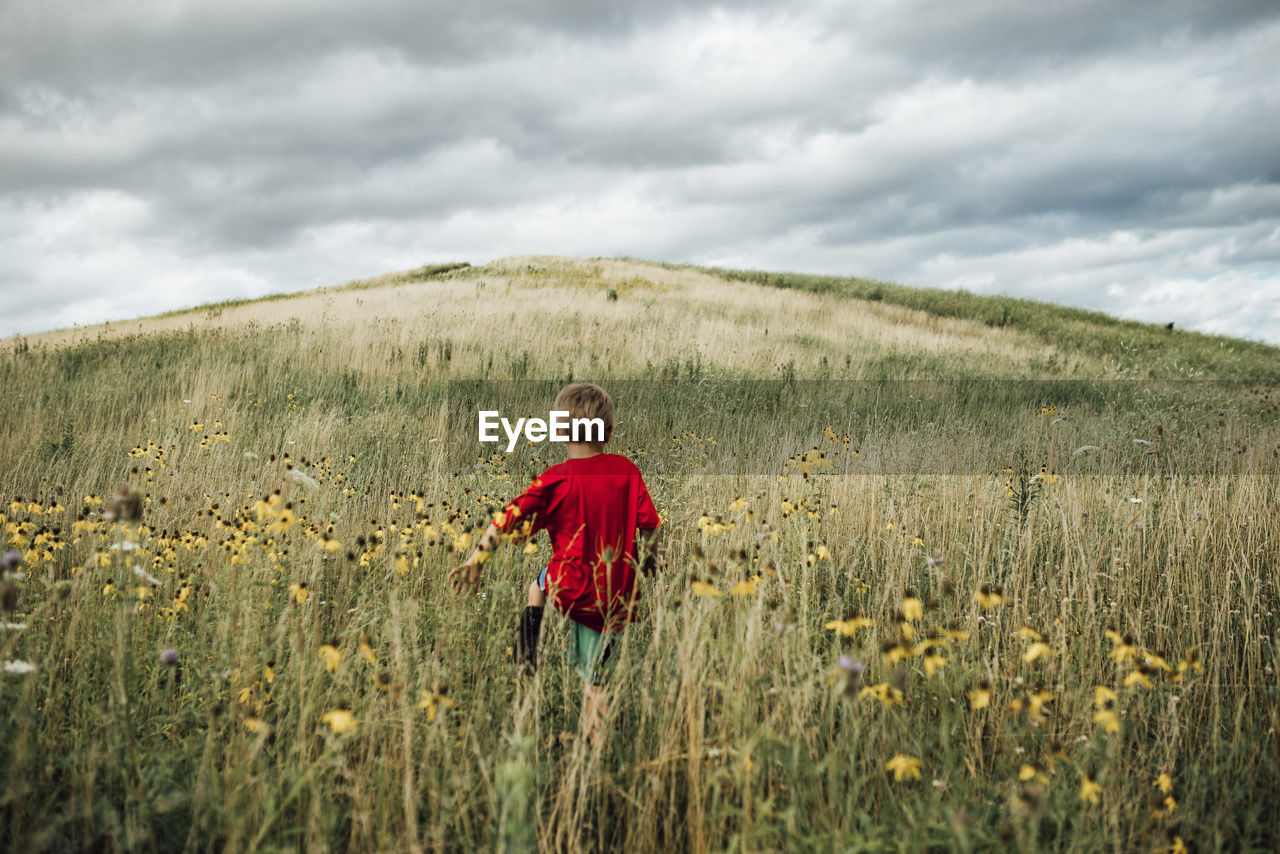 Rear view of boy walking on grassy field against cloudy sky