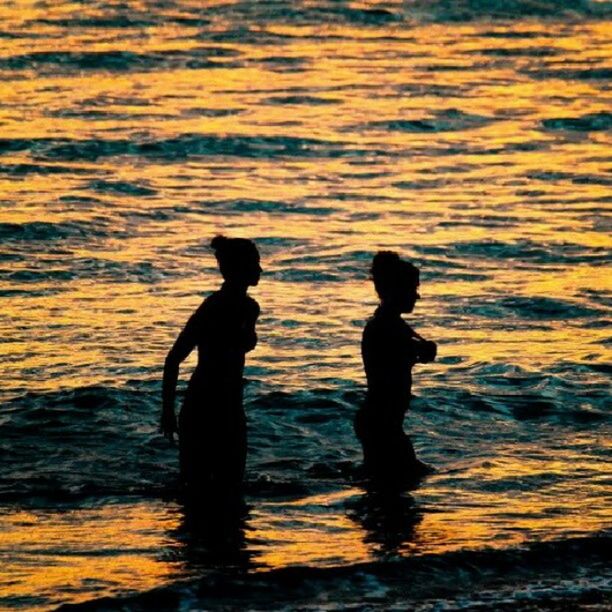 SILHOUETTE OF PEOPLE IN SEA AT SUNSET