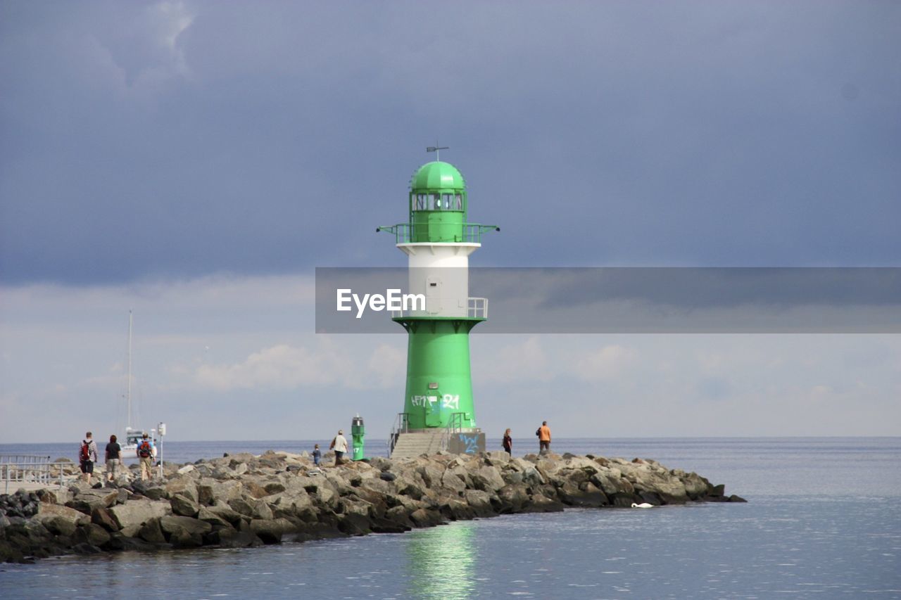 People and lighthouse by sea against sky