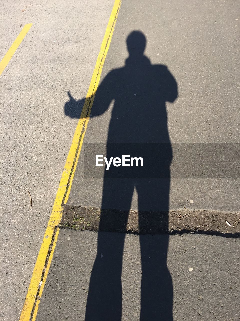 Shadow of man hitchhiking on road