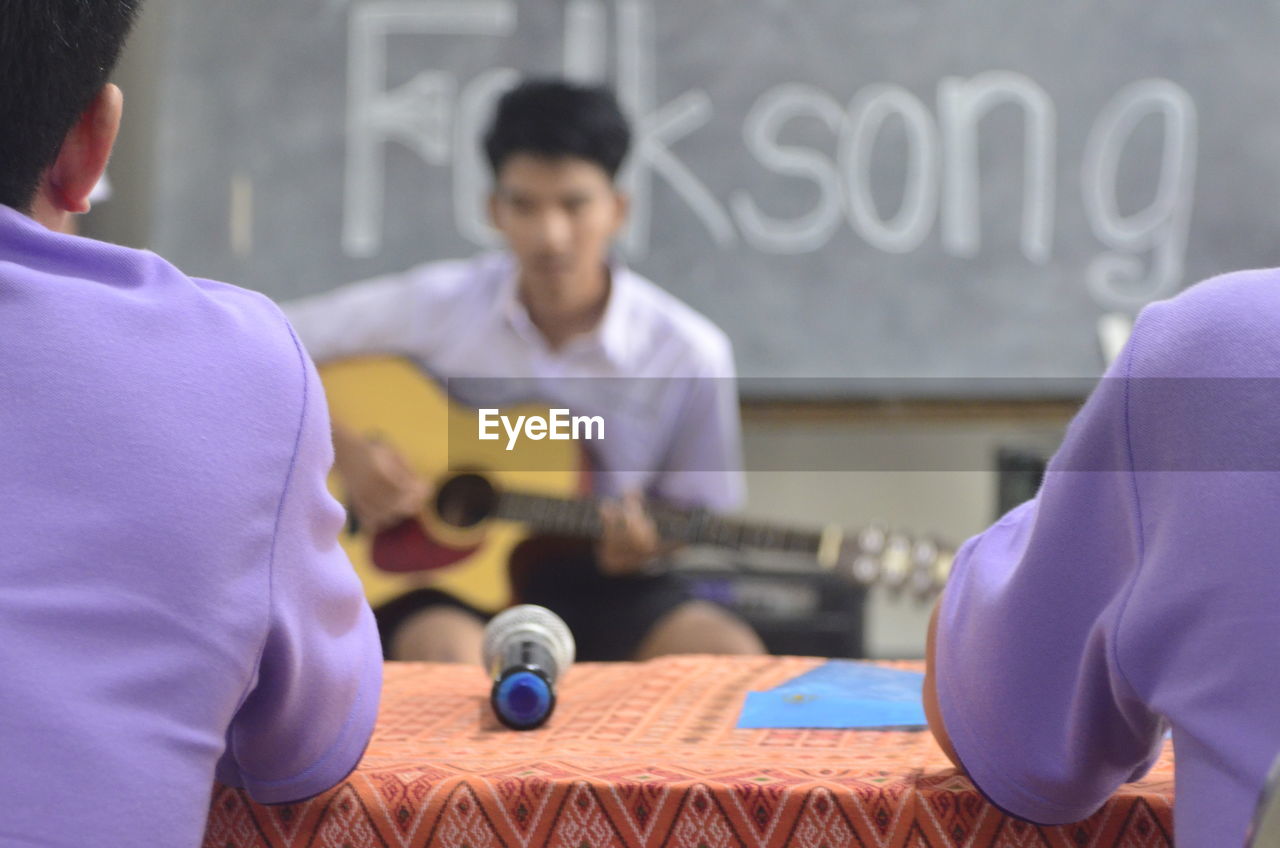 Rear view of judges listening to male contestant playing guitar during competition