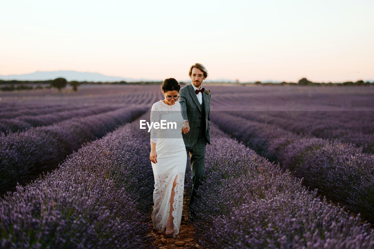 Bride and groom holding hands and walking in blossoming lavender field