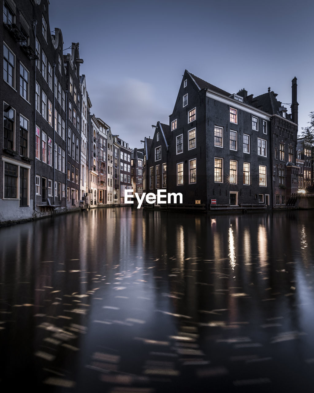 Illuminated buildings by river against sky in city