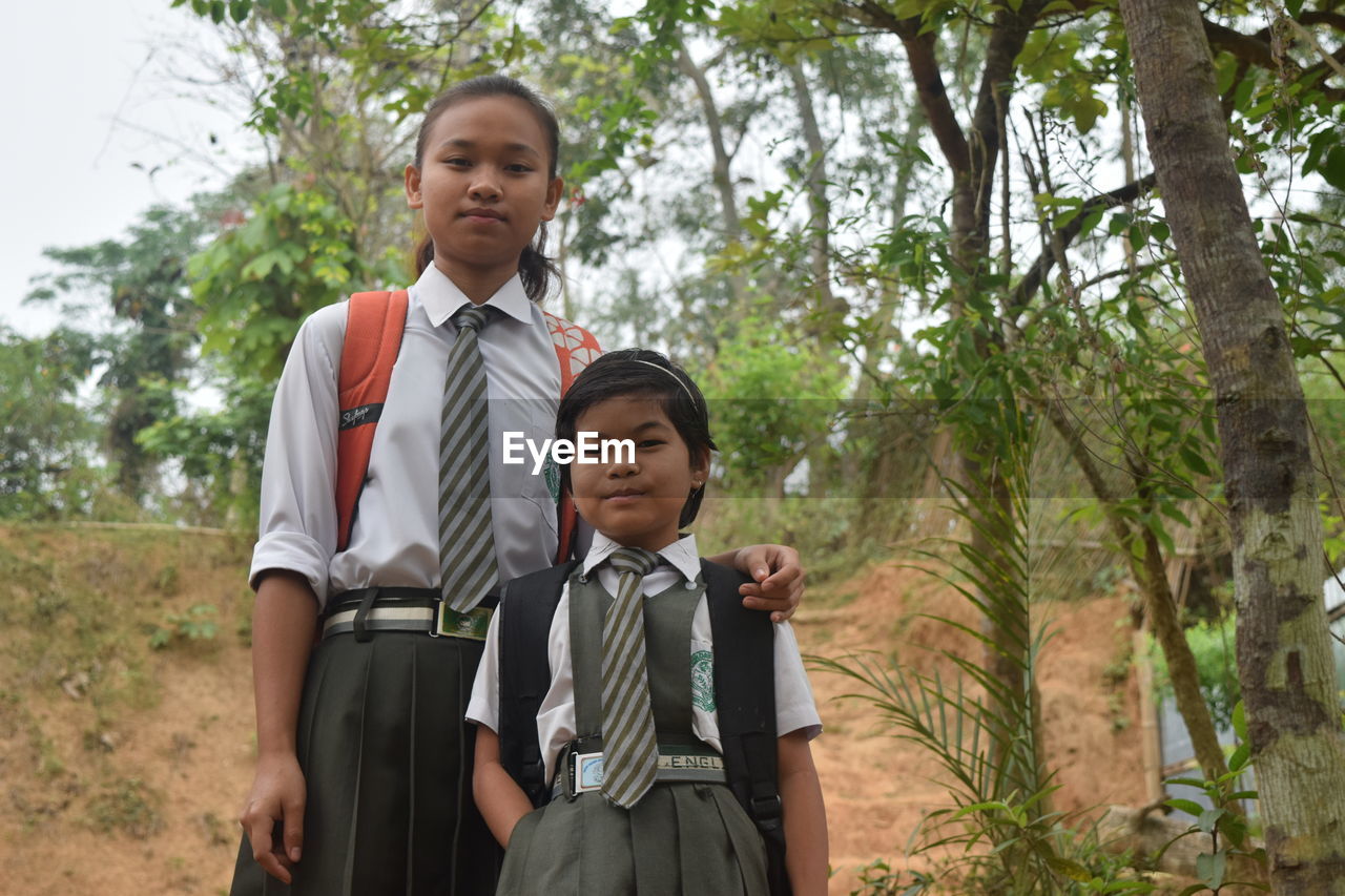 Portrait of sisters in school uniform standing against trees