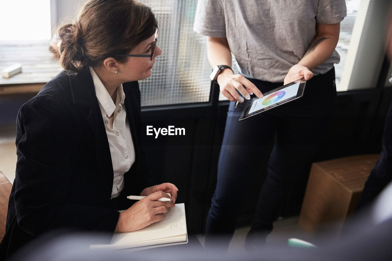 Midsection of creative businesswoman explaining female bank manager over digital tablet in office