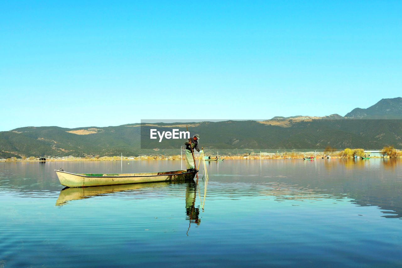 Fisherman sailing on boat against clear blue sky