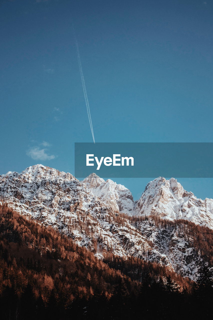 Low angle view of snowcapped mountains against blue sky