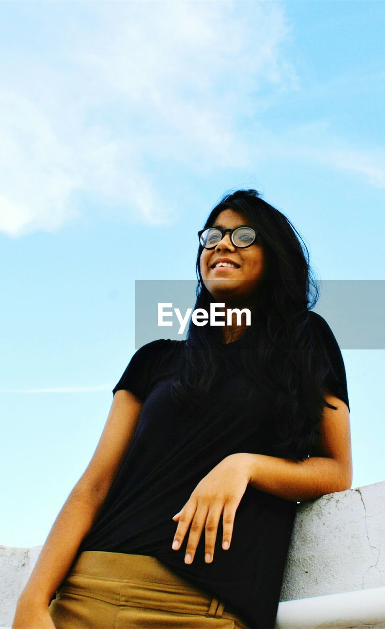 Low angle view of young woman standing by retaining wall against sky