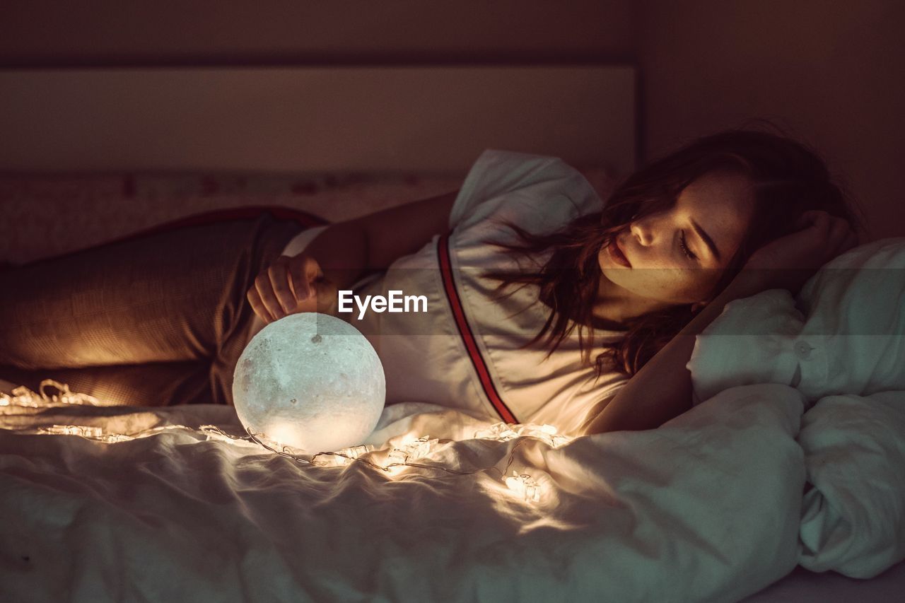 Woman sleeping with sphere and fairy lights on bed at home