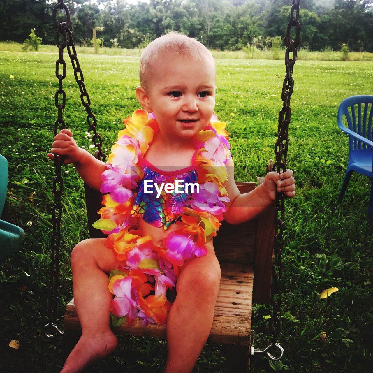 Cute baby girl wearing floral garland sitting on swing in park