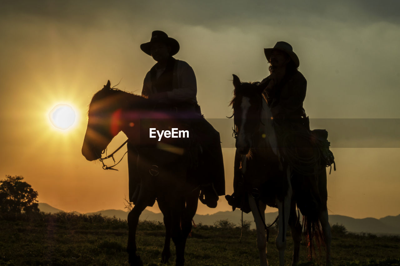 MEN RIDING HORSES ON FIELD DURING SUNSET