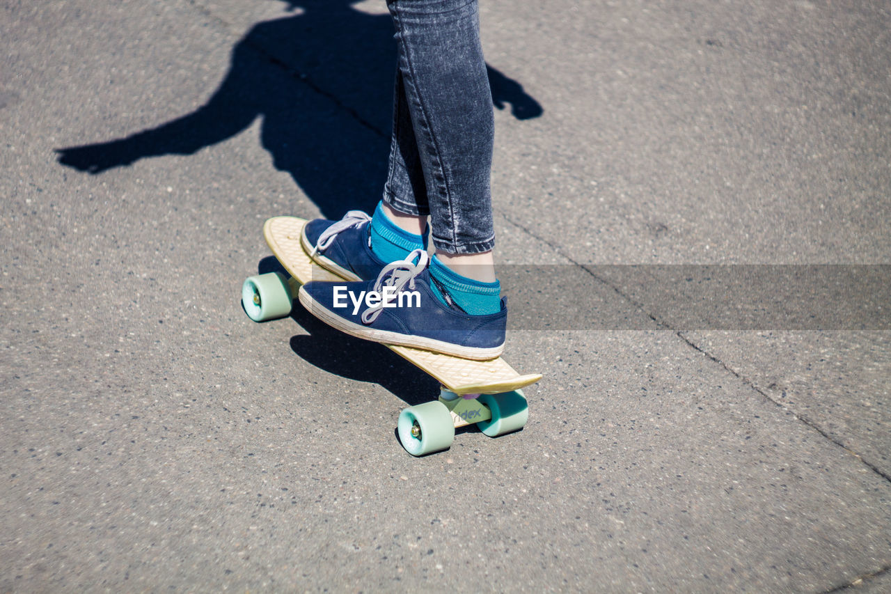 Low section of woman skateboarding on road