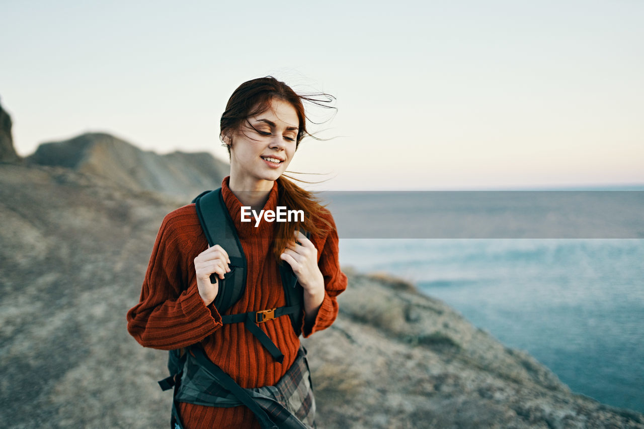 BEAUTIFUL YOUNG WOMAN STANDING AGAINST SEA AND SKY