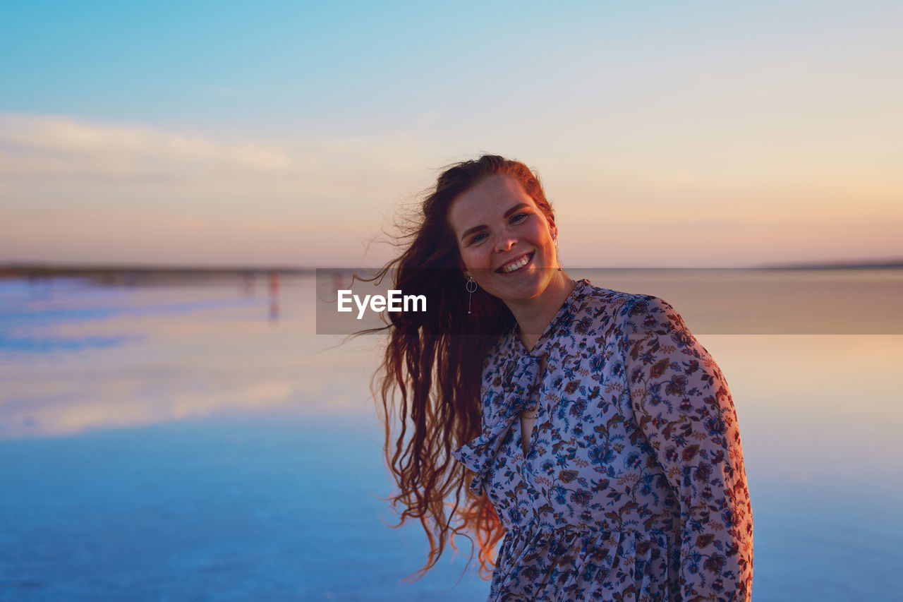 Beautiful young woman with flying red hair on the ocean coast at sunset time person