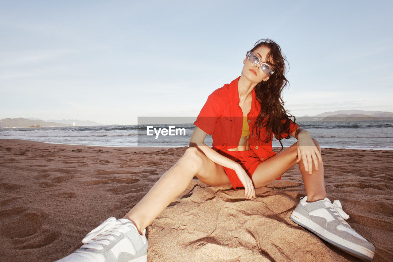 young woman sitting on beach against sky