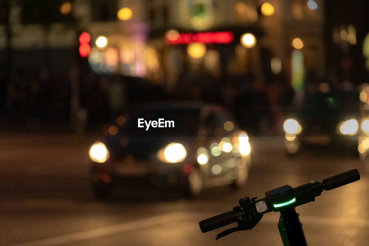 Electric pushscooter and cars on illuminated city street at night