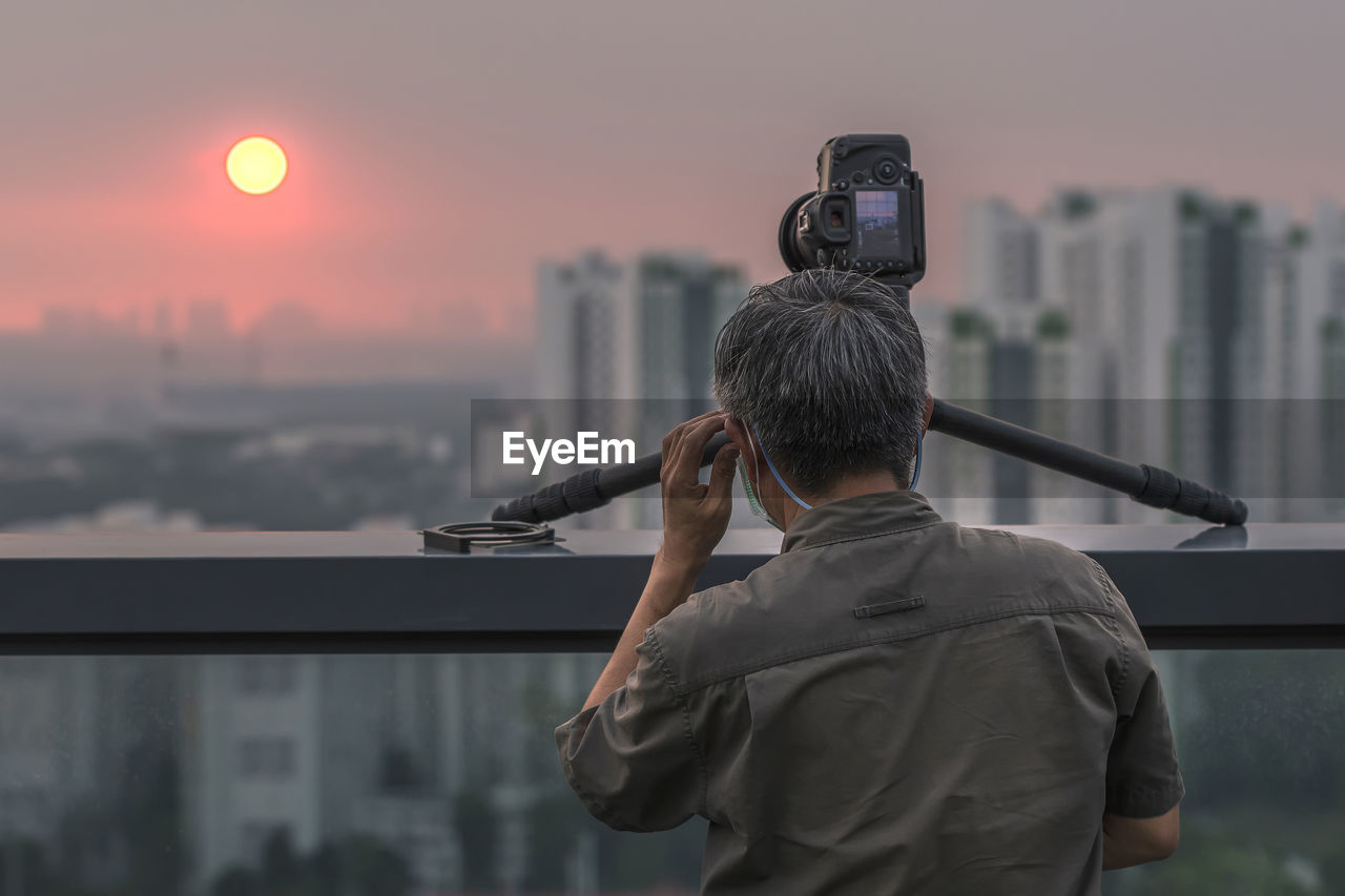 REAR VIEW OF MAN PHOTOGRAPHING AGAINST CITYSCAPE