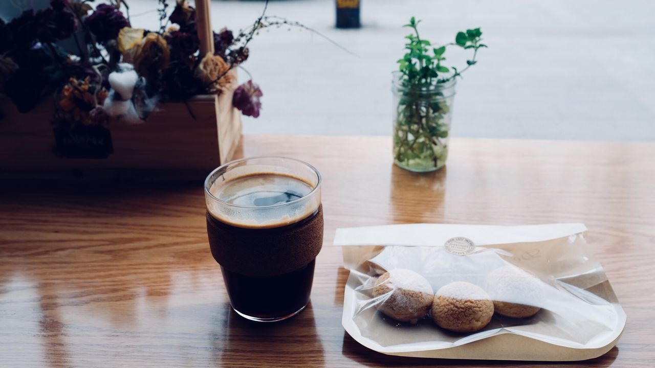 CLOSE-UP OF COFFEE CUP AND CHOCOLATE ON TABLE BY GLASS