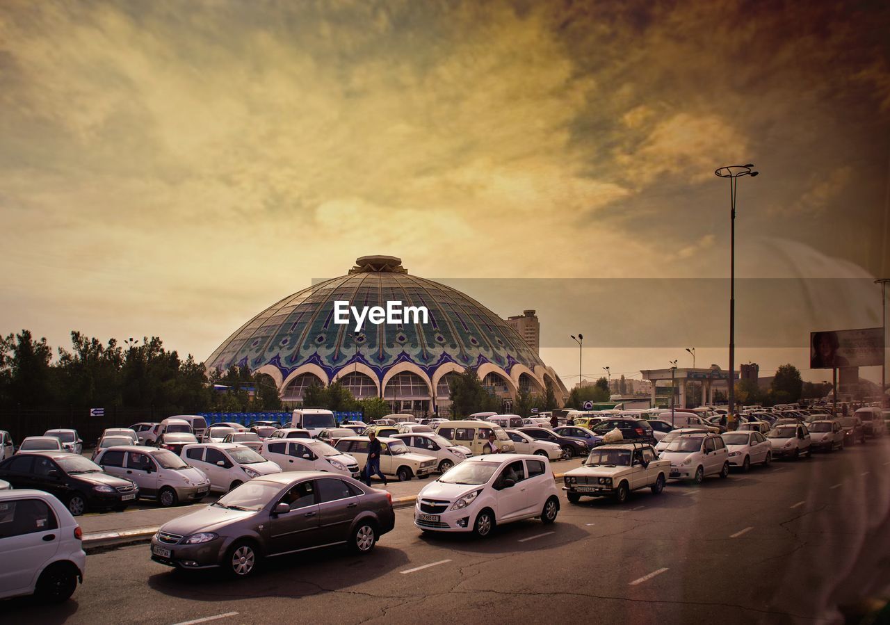 Vehicles on road against buildings at sunset