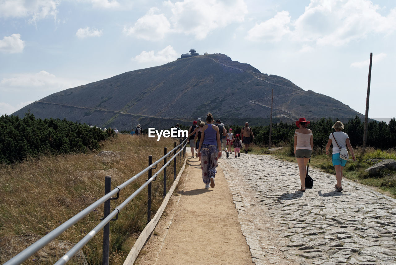 PEOPLE WALKING ON MOUNTAIN BY ROAD AGAINST SKY