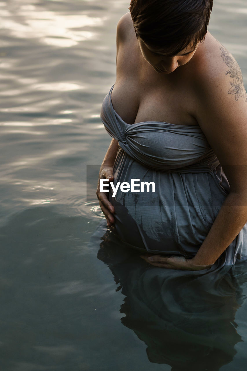 Midsection of pregnant woman standing by lake