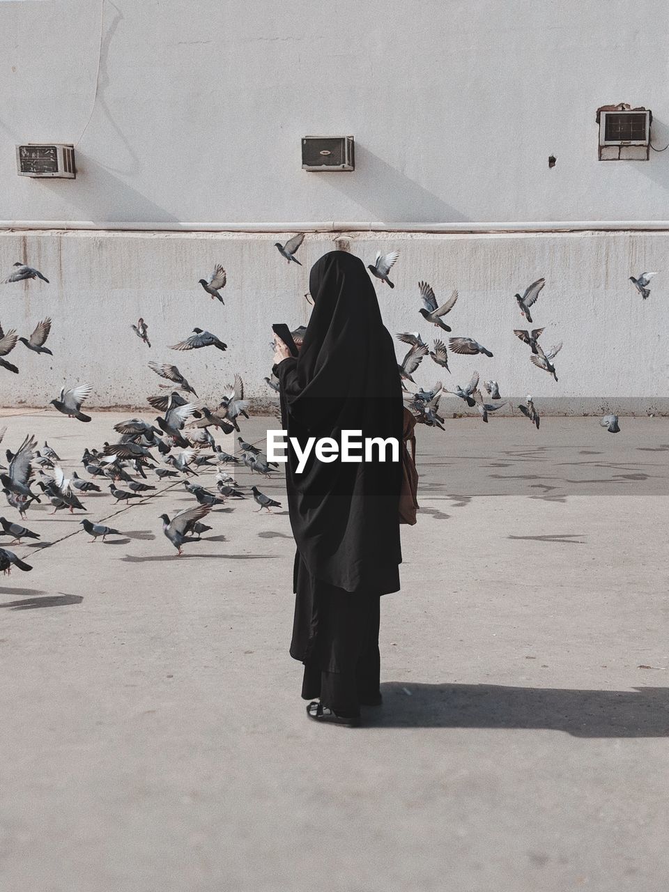 Woman standing in burka against pigeons on footpath