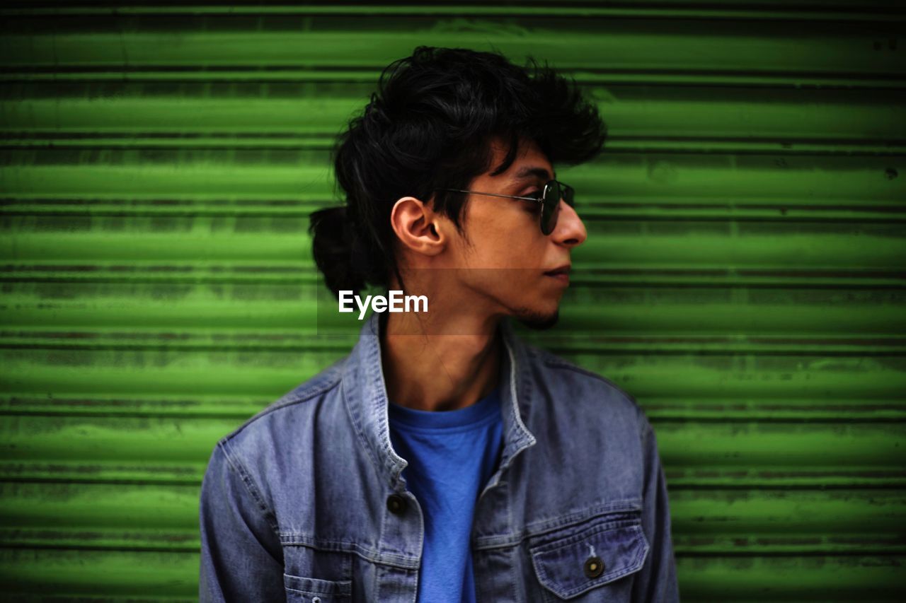 Young man looking away while standing against shutter 