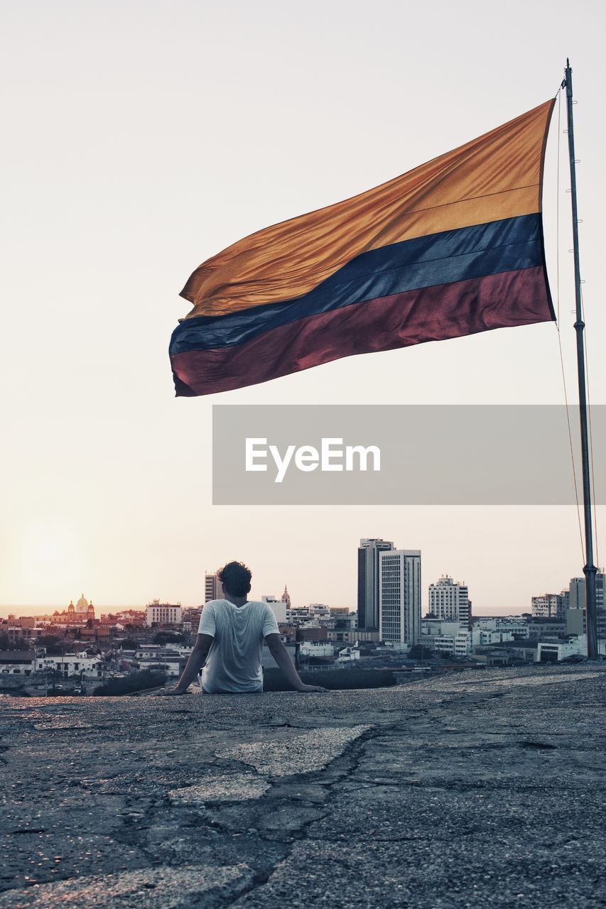 Rear view of man sitting by flag against clear sky