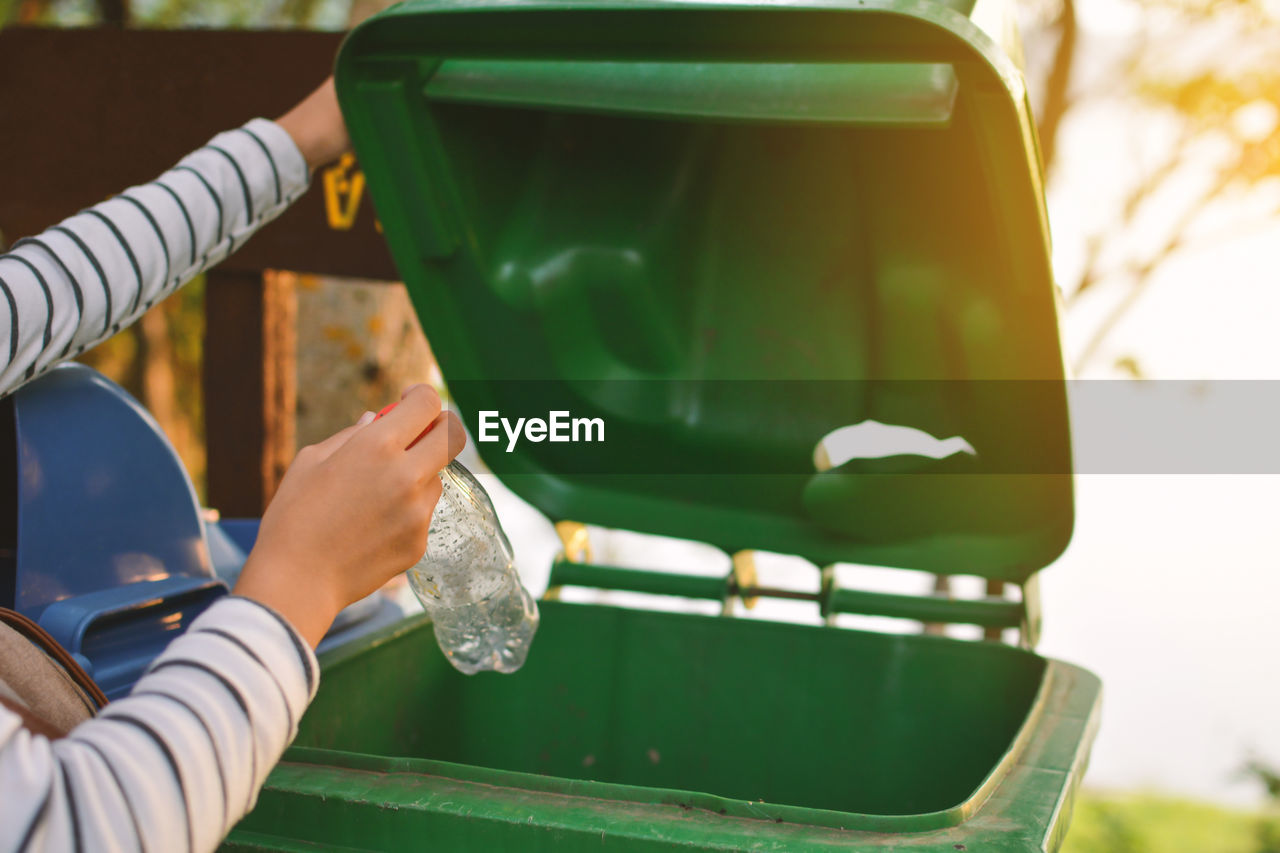 Cropped hands of person throwing bottle in garbage bin