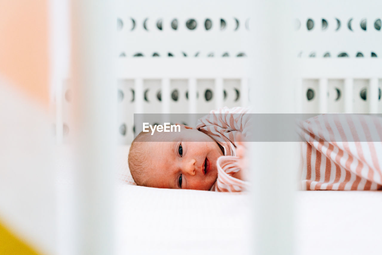 Straight on portrait of a baby girl laying in her modern crib