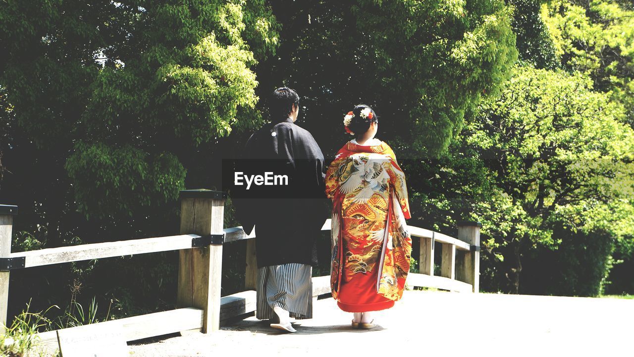 Rear view of couple in traditional clothing walking on footbridge by trees