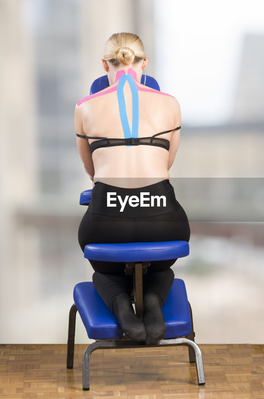 Rear view of mature woman with pink kinesio tape sitting on neck massage chair