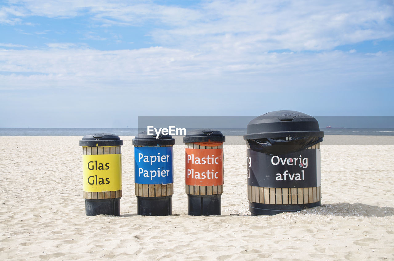 Recycling trash cans on beach against sky