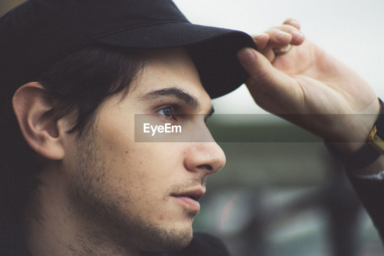 Close-up of young man looking away while holding cap