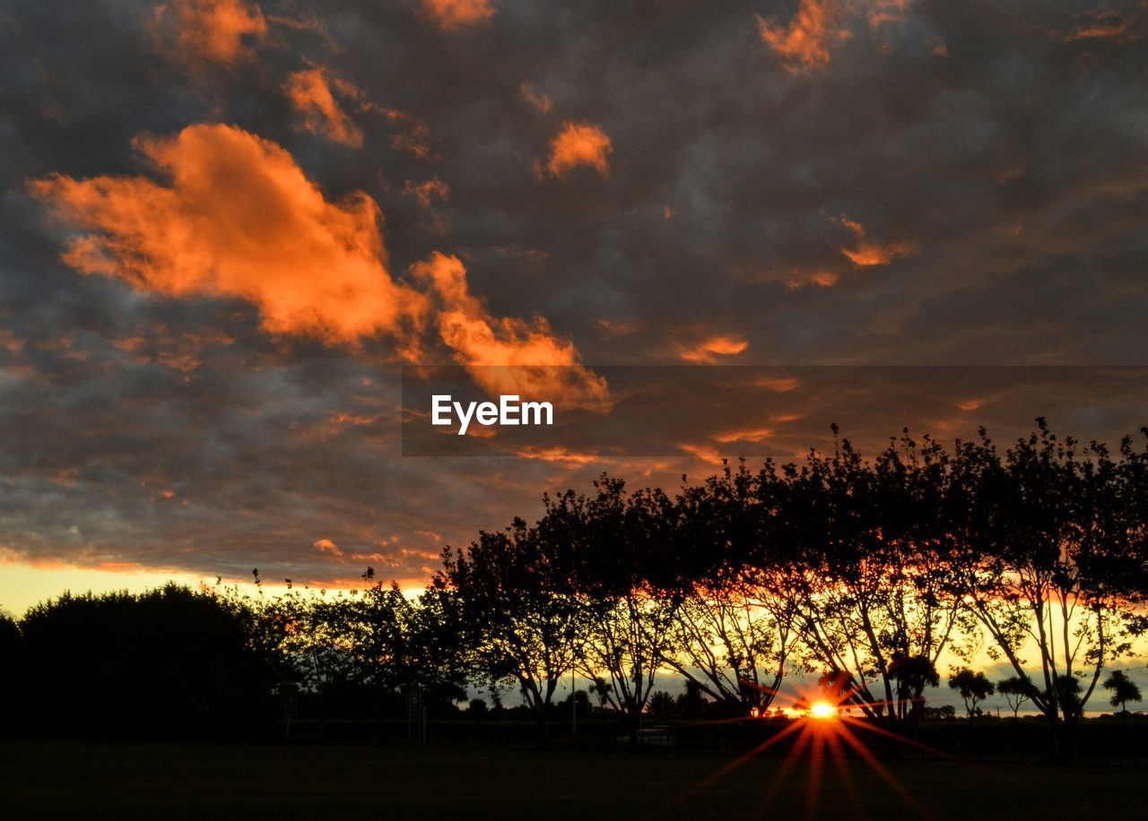 Silhouette of trees on landscape against cloudy sky