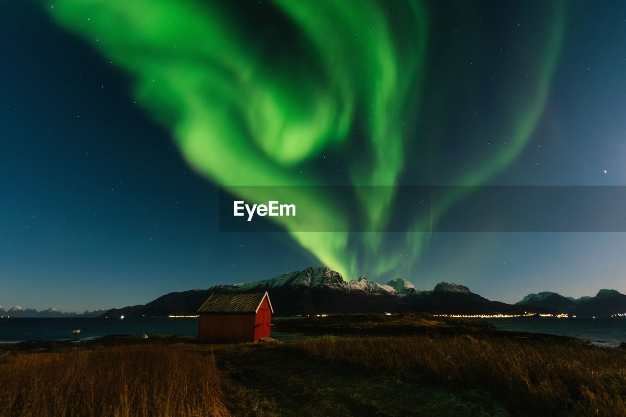Scenic view of red building against snowcapped mountains and northern lights at night