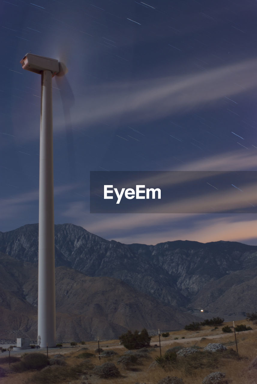 Low angle view of moving wind turbine against star trails on field