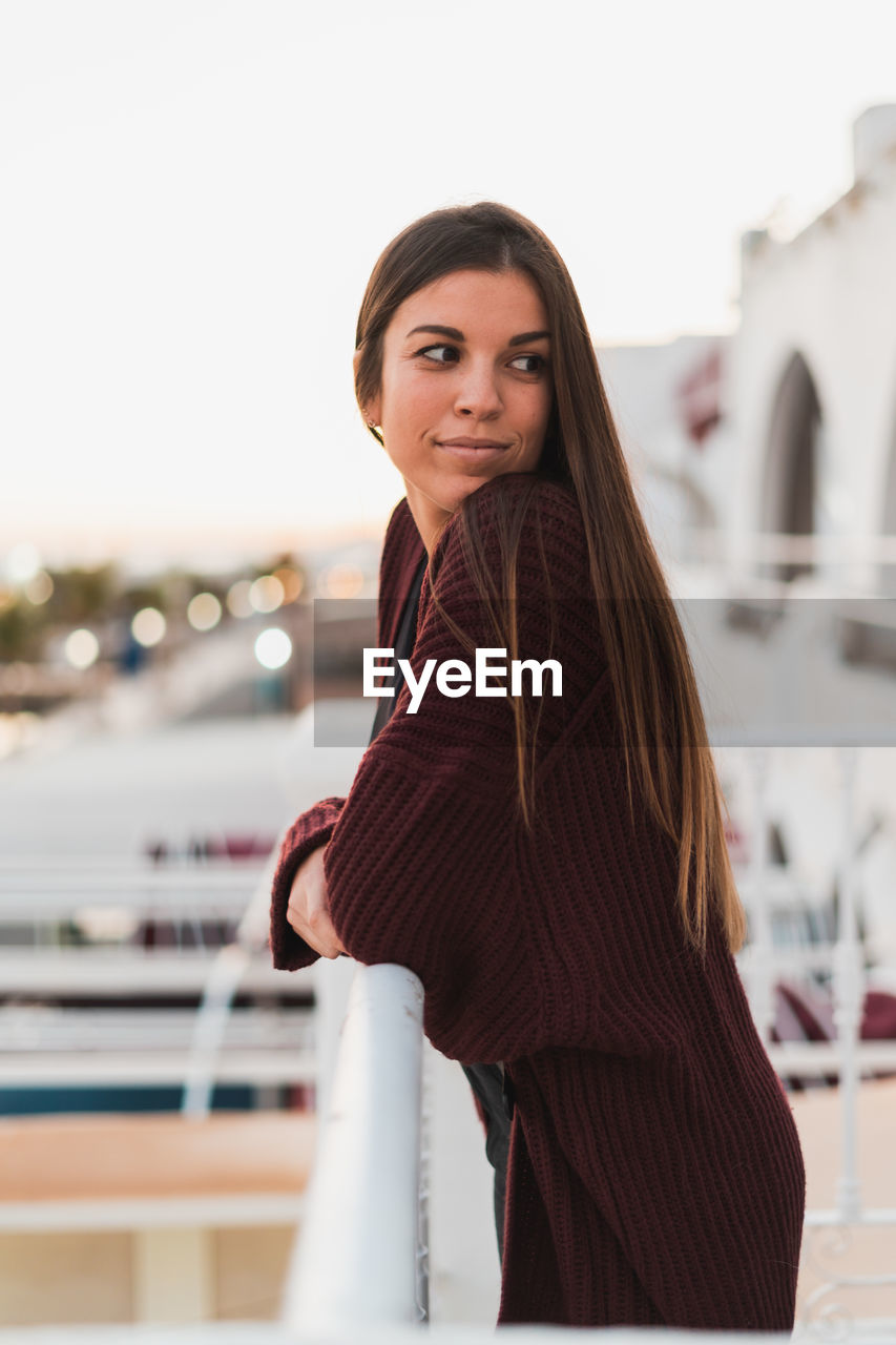 Side view of thoughtful woman standing at railing against clear sky