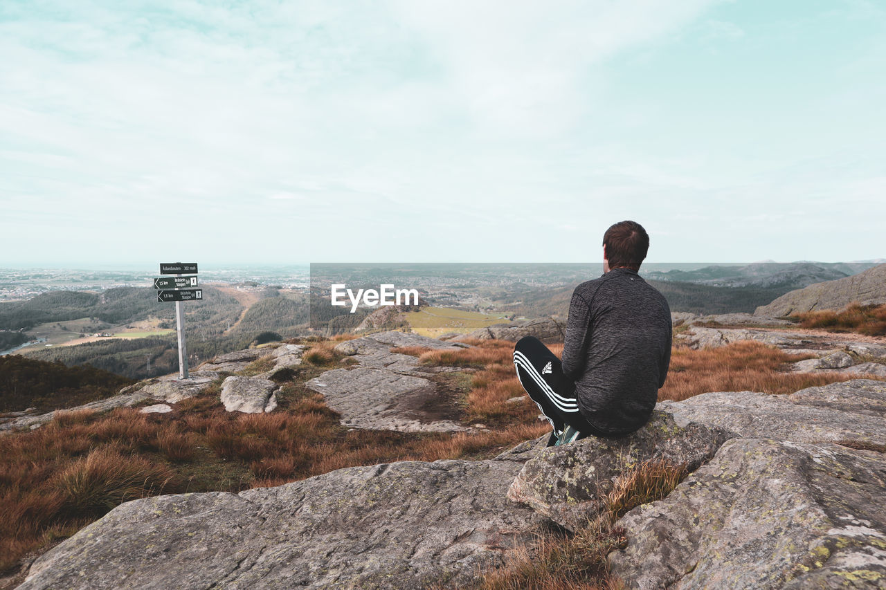 REAR VIEW OF MAN SITTING ON ROCK