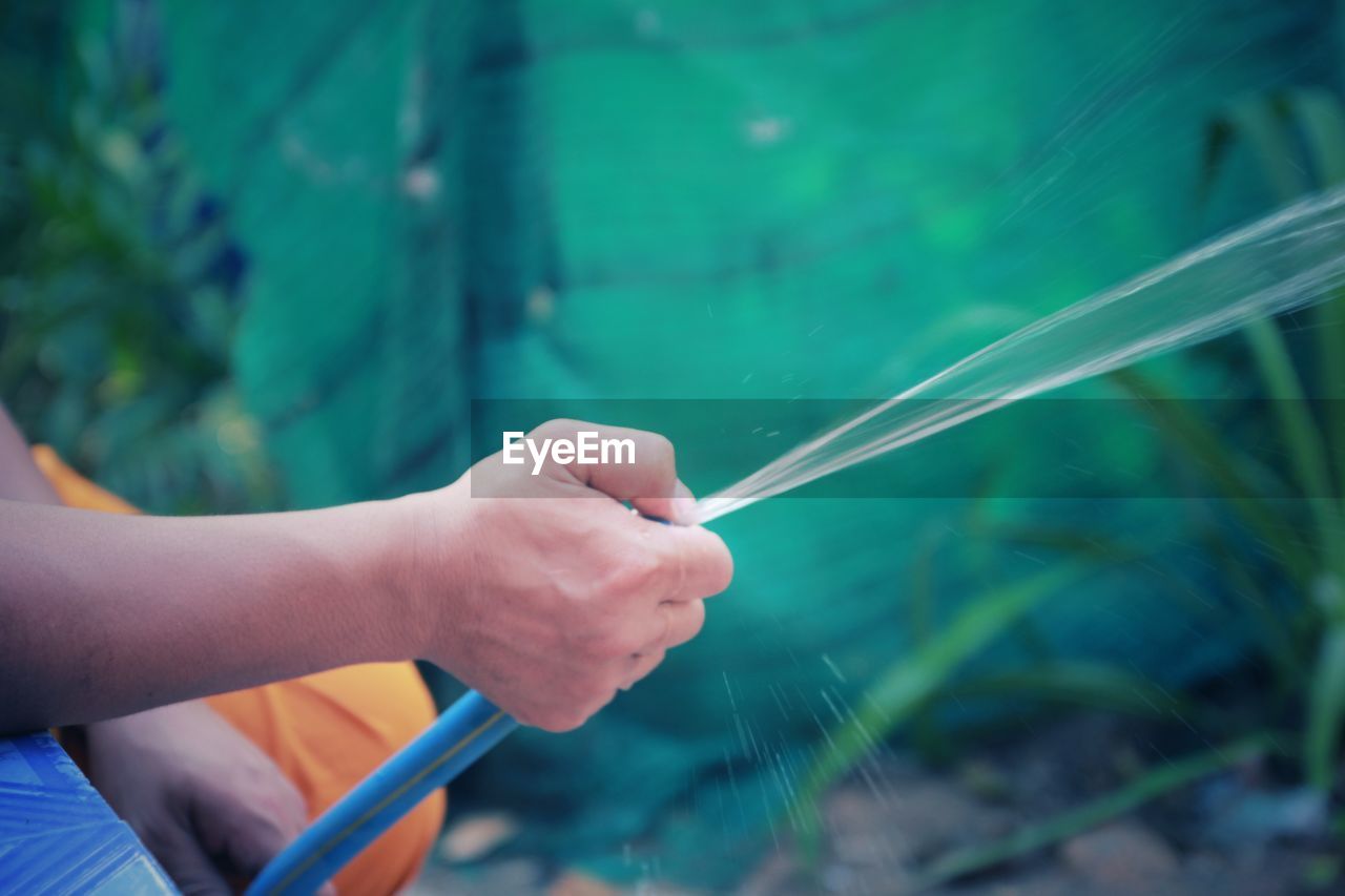 Cropped hand of man spraying water through pipe