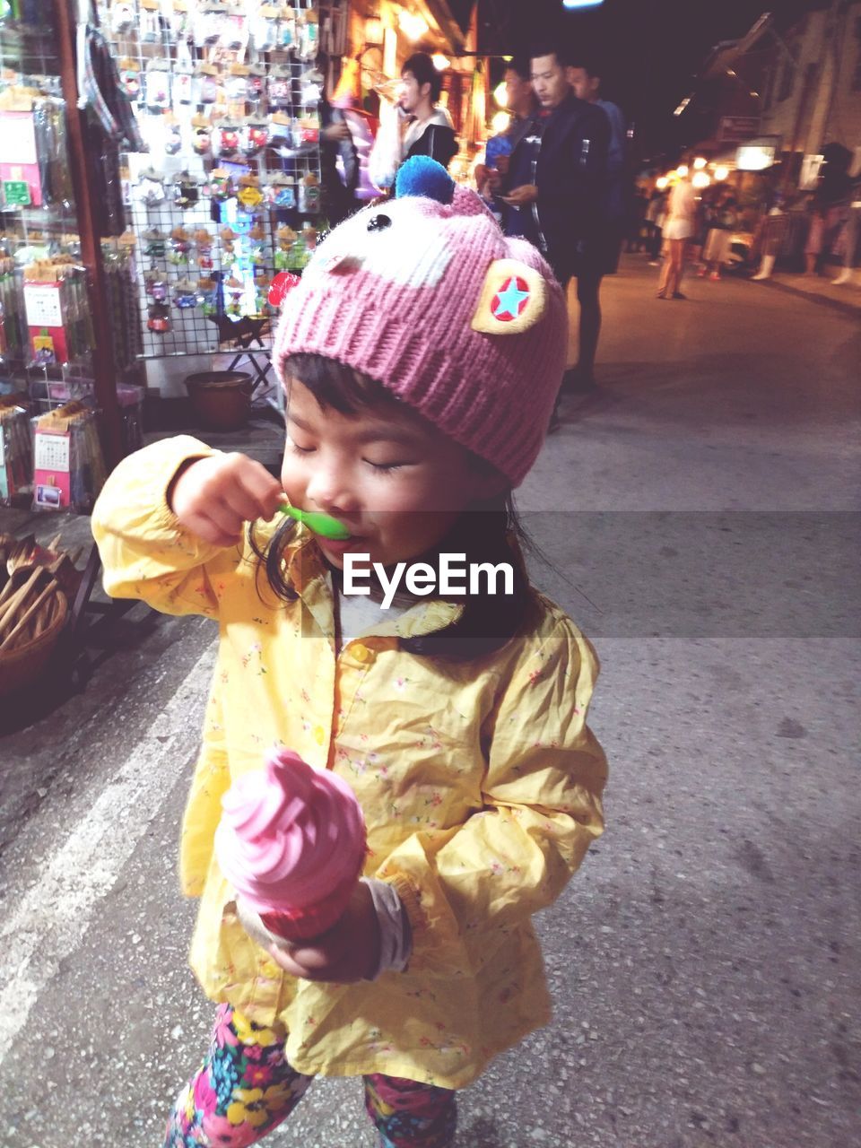 Cute girl eating ice cream while standing on street in city at night